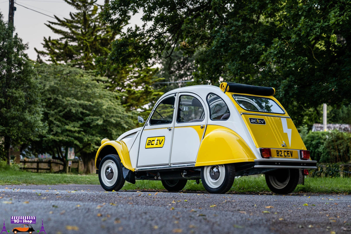 The yellow and white 2cEv electric Citroën 2CV parked on a tree-lined road